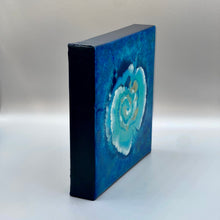 Load image into Gallery viewer, Half-profile on an iridescent metallic painting with blue spiral flower with accents of pearl white and gold. Painted on an 8 inch by 8 inch gallery wrapped cotton canvas that is 1.5 inch thick. Finished with resin to make it look like it&#39;s under glass.
